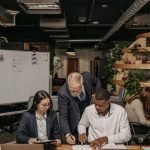 A diverse team collaborating at a table with laptops and documents in a modern office environment.